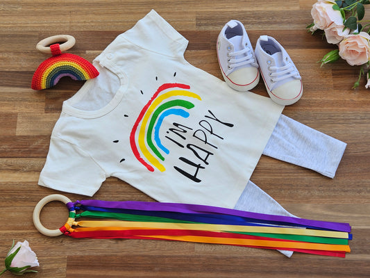 White T_Shirt with rainbow image, grey organic cotton leggings, white jogger shoe, rainbow rattle + ribbon teether ring